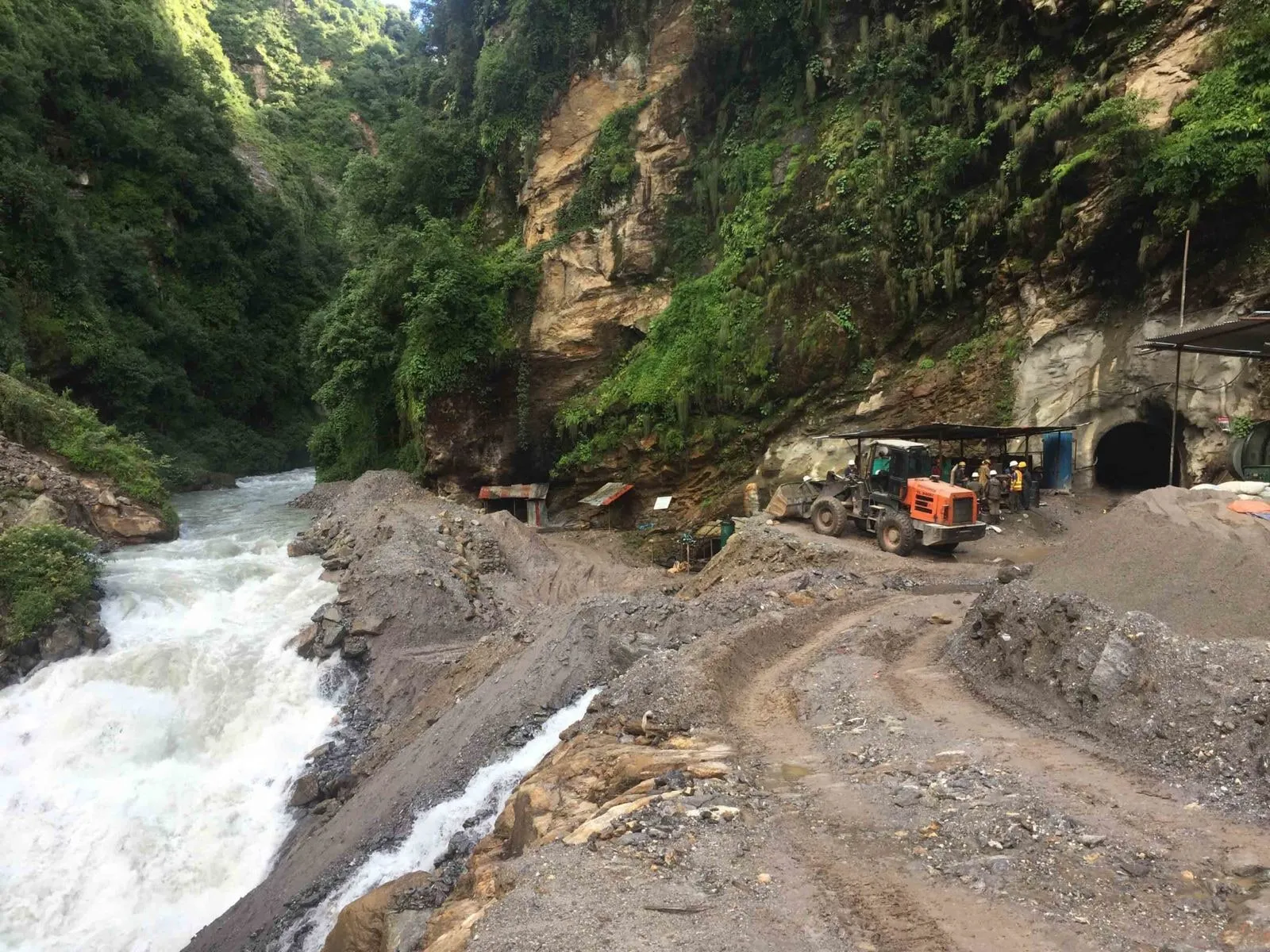 Access road cut into a forested river gorge, with a support vehicle and works crew