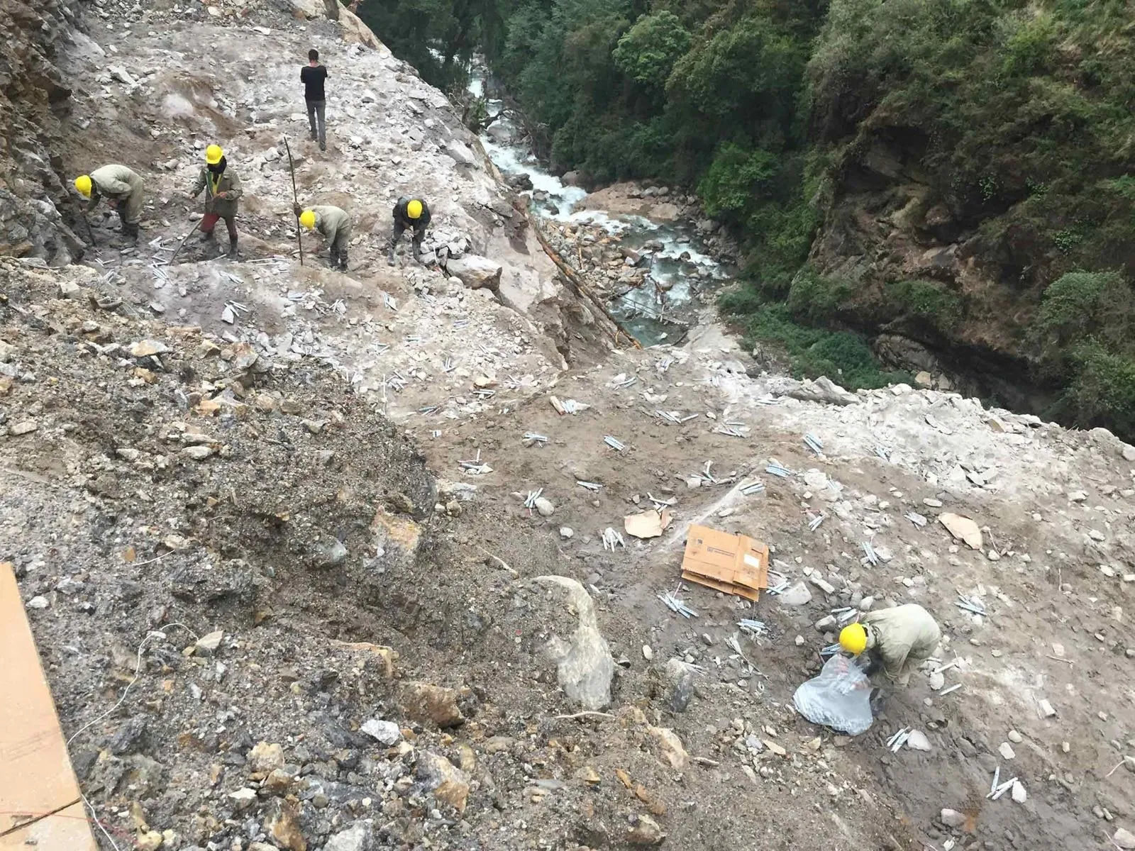 Workers in hard hats on a steep slope above the river, clearing material by hand