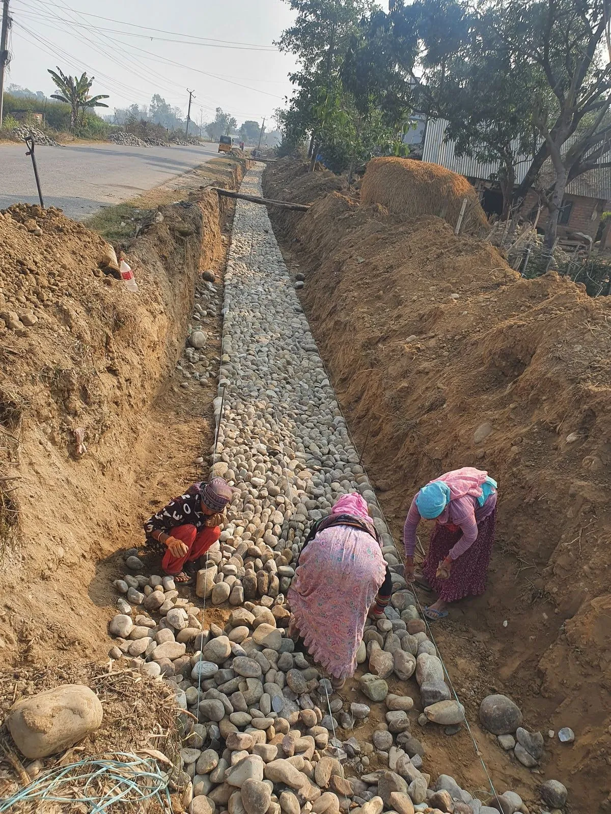 Roadside drainage channel under construction, workers placing stone lining